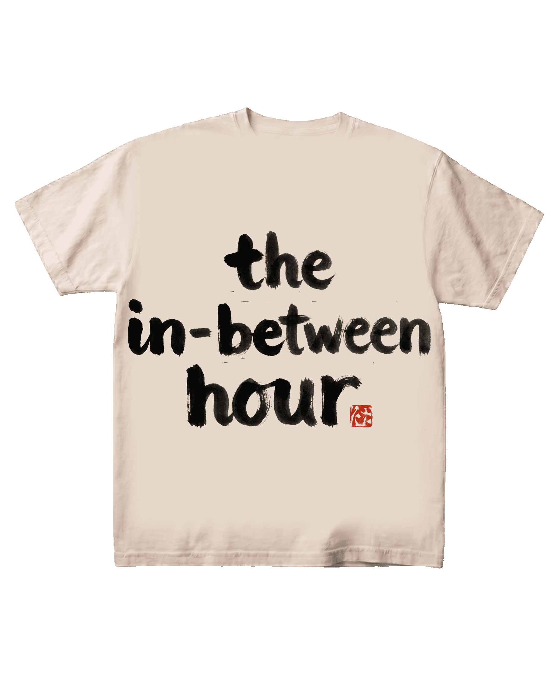The 'the in-between hour' typographic tee on a pure black background, flat-front catalog presentation. Hand-brushed sumi-e ink lettering centered on the chest with a vermilion hanko seal mark.