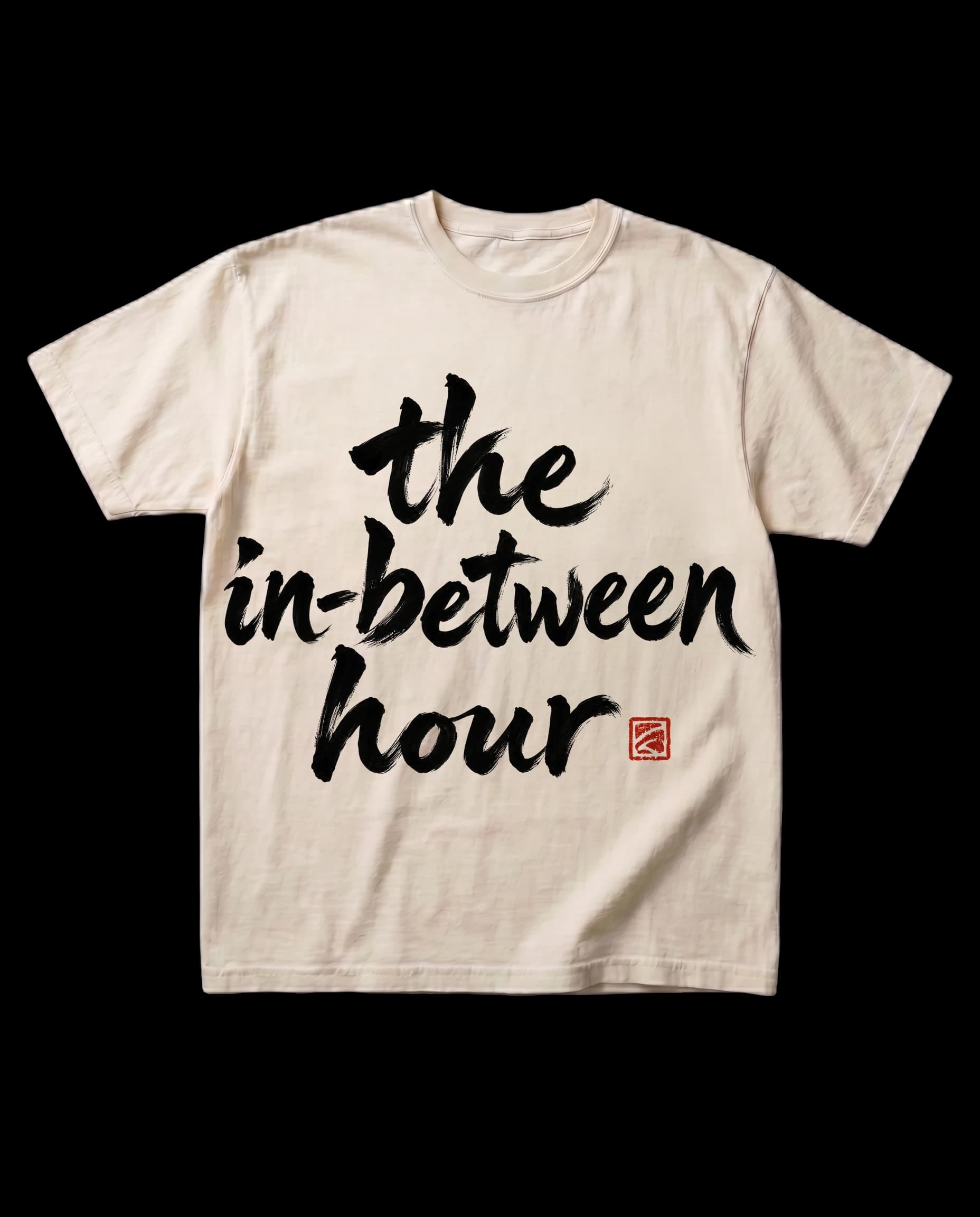 The in-between hour tee in Bone, laid flat: the words 'the in-between hour' brushed in sumi-ink calligraphy, with a small red seal.