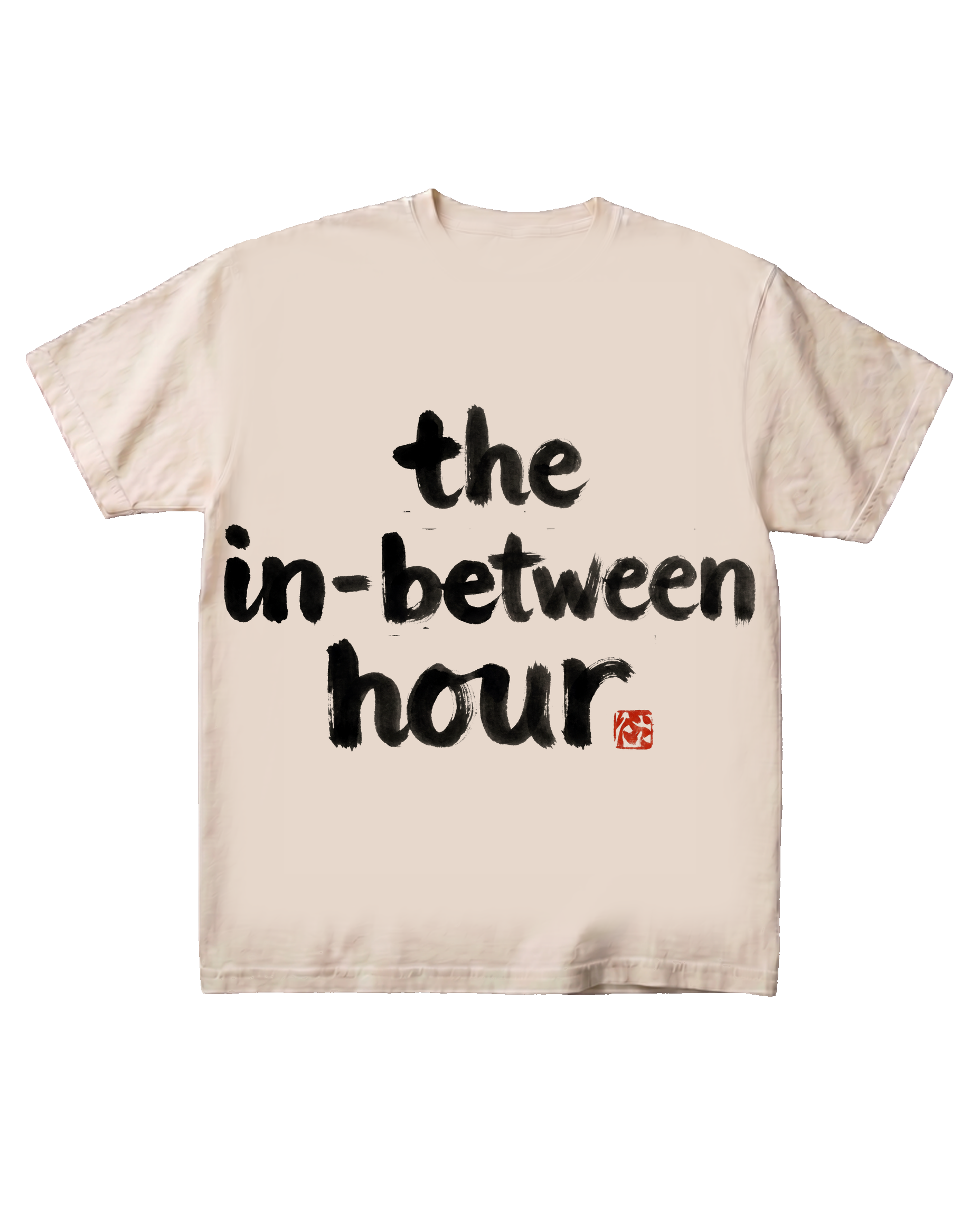The 'the in-between hour' typographic tee on a pure black background, flat-front catalog presentation. Hand-brushed sumi-e ink lettering centered on the chest with a vermilion hanko seal mark.